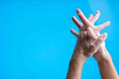 Mavi arka planda sabun köpüğü kullanarak ellerini yıkıyor. Kovid19, Bakteri ve sağlık hizmetleri kavramından korunma.