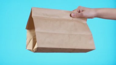 Mavi arka planda izole edilmiş paket servis vermek için kahverengi el işi kağıt torbasıyla kadın elini kapat. Paketleme şablonu maketi. Teslimat hizmeti konsepti. Uzayı kopyala Reklam alanı