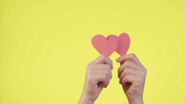 Las hembras sostienen en las manos pequeños corazones rojos aislados sobre fondo amarillo. Concepto de ternura en redes sociales. Día de San Valentín mujeres internacionales — Vídeos de Stock