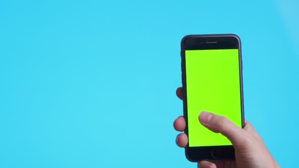 Рука жінки, що тримає чорний смартфон з зеленим екраном, торкаючись або прес-дисплеєм, людина використовує мобільний телефон з сенсорним дисплеєм клавіш хроми на синьому фоні . — стокове відео
