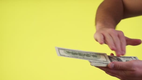 Руки кидають долари, розсіюючи гроші, витрачаючи гроші недбало. закритий студійний знімок ізольований на жовтому фоні — стокове відео