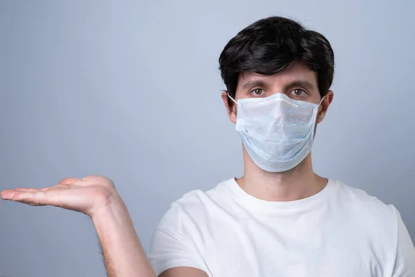 Uomo in maschera medica che mostra e presenta con mano aperta palmo su uno sfondo grigio . — Foto Stock