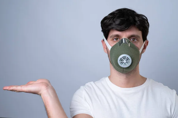 Man in a respirator showing and presenting with open hand palm on a gray background. — Stock Photo, Image