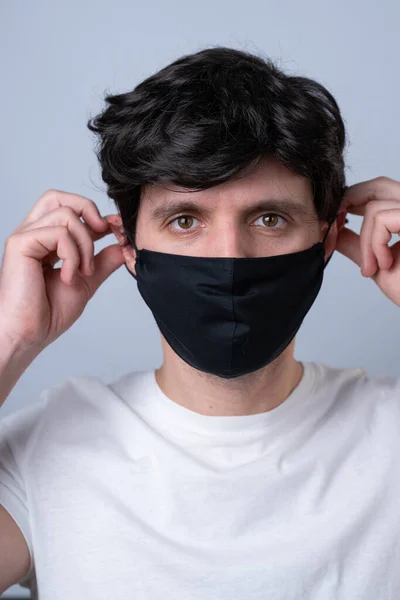 Mann setzt ihr vor grauem Hintergrund eine schwarze medizinische Maske auf — Stockfoto