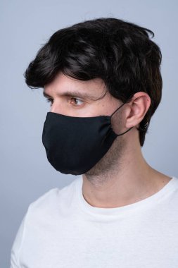 Siyah tıbbi maskeli bir adam, gri bir arka planda izole edilmiş.