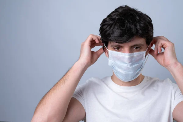 Homem coloca uma máscara médica em seu rosto em um fundo cinza — Fotografia de Stock