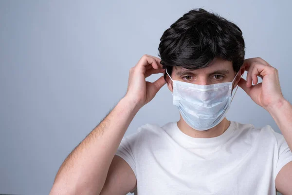 L'uomo le mette una maschera medica sul viso su uno sfondo grigio — Foto Stock