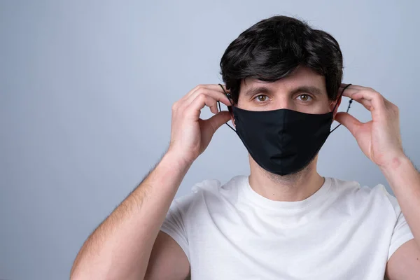 Man puts a black medical mask on her face on a gray background — Stock Photo, Image