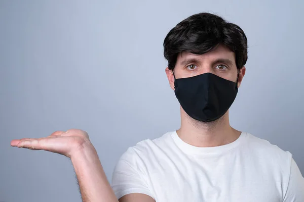 Homem em uma máscara médica preta mostrando e apresentando com palma da mão aberta em um fundo cinza . — Fotografia de Stock