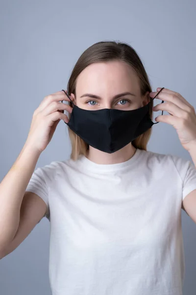 Woman puts a black medical mask on her face on a gray background — Stock Photo, Image