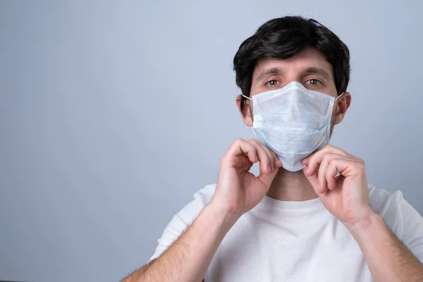 Homem coloca uma máscara médica em seu rosto em um fundo cinza — Fotografia de Stock