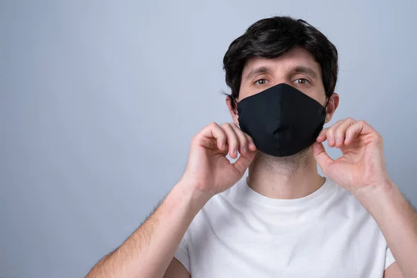 Man puts a black medical mask on her face on a gray background — Stock Photo, Image