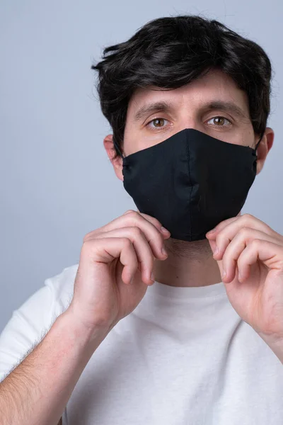 Homem coloca uma máscara médica preta em seu rosto em um fundo cinza — Fotografia de Stock