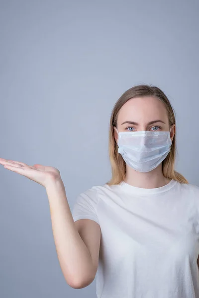 Uma mulher em uma máscara médica mostrando e apresentando com palma da mão aberta em um fundo cinza . — Fotografia de Stock
