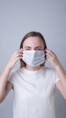 Dikey video. Kadın yüzüne gri bir arka plan takıyor.