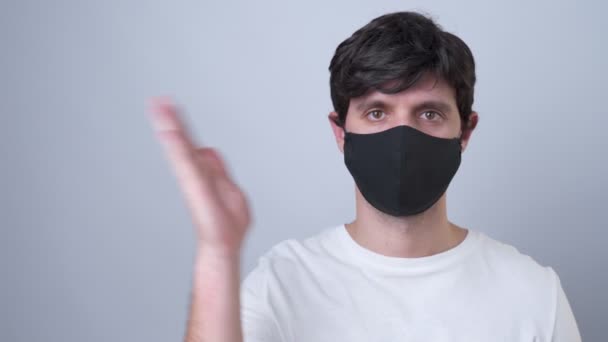 Homem em uma máscara médica preta mostrando e apresentando com palma da mão aberta em um fundo cinza . — Vídeo de Stock