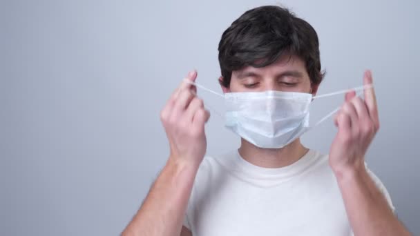 Le portrait en gros plan d'une femme enlève un masque médical pendant la quarantaine du coronavirus du virus COVID-19. Sur fond gris — Video