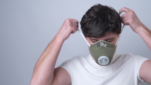 Close-up portrait of a man removes a respiratory face mask during the quarantine of the COVID-19 virus coronavirus. On a grey background — Stock Video