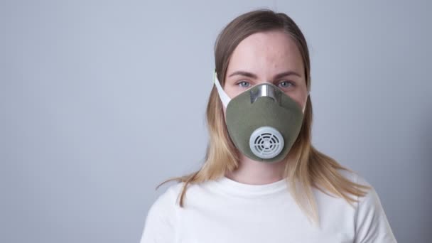 Close-up portrait of a woman removes a respiratory face mask during the quarantine of the COVID-19 virus coronavirus. On a grey background — Stock Video