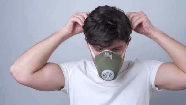 Az ember egy légzőmaszkot tesz az arcára szürke alapon. — Stock videók