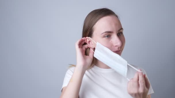 Mujer pone una máscara médica en su cara sobre un fondo gris — Vídeos de Stock