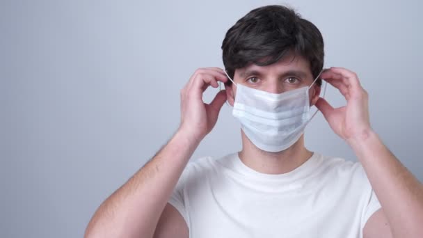 Мужчина надевает медицинскую маску на её лицо на сером фоне — стоковое видео