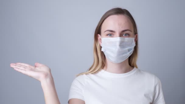 Donna in maschera medica che mostra e presenta con mano aperta palmo su uno sfondo grigio . — Video Stock