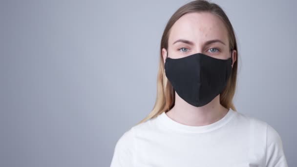 Женщина в черной медицинской маске, изолированная на сером фоне — стоковое видео