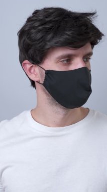 Dikey video. Siyah tıbbi maskeli bir adam, gri bir arka planda izole edilmiş.