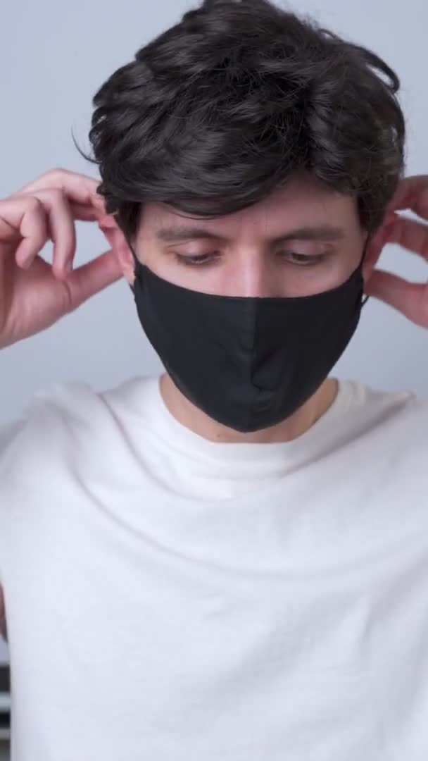 Verticale video. man zet een zwart medisch masker op haar gezicht op een grijze achtergrond — Stockvideo