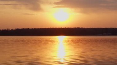 Sakin göl ve ormanın üzerinde güneş batıyor.
