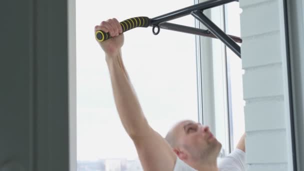 Мужчина занимается спортом, делая упражнения на горизонтальной панели у себя дома — стоковое видео