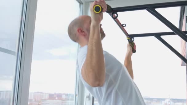 Мужчина занимается спортом, делая упражнения на горизонтальной панели у себя дома — стоковое видео