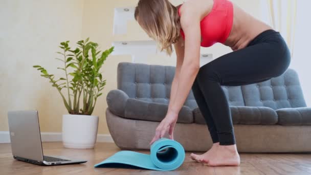 Frau rollt Fitness- oder Yogamatte vor dem Sport, trainiert zu Hause im Wohnzimmer oder im Yogastudio. Gesunde Gewohnheiten, Fitness, Konzepte zur Gewichtsreduktion. — Stockvideo