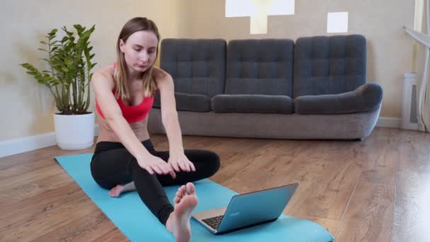 Slim desportista no sportswear aquecimento-up músculos antes do treino fazendo alongamento exercício sentado no chão em casa — Vídeo de Stock