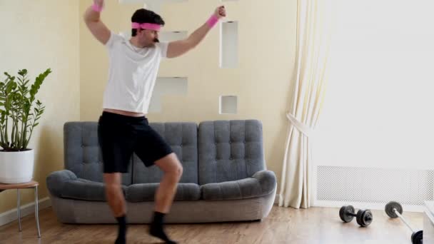Vicces hülye kinézetű fitness férfi táncol élvezi a zenét, és bemelegítés edzés a nappaliban. — Stock videók