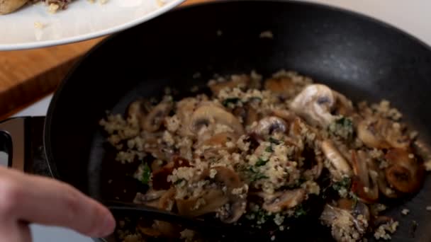 Vrouw zet quinoa en champignons op een bord — Stockvideo