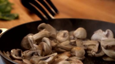 Ahşap spatulası olan bir kadının yakın plan çekimi tavada doğranmış şampiyon mantarlarına engel oluyor. Yavaş çekim videosu