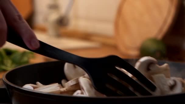 Крупный план женщины с деревянной лопаткой мешает нарезанным шампиньонам на сковороде. Видео замедленного действия — стоковое видео
