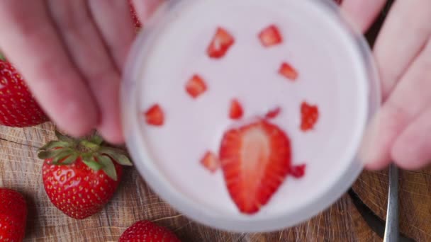 Una donna mette una ciotola di yogurt alla fragola sul tavolo da pranzo con le mani. La vista dall'alto — Video Stock