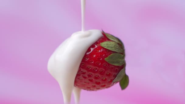 Sahne wird über eine Erdbeere auf rosa Hintergrund gegossen — Stockvideo