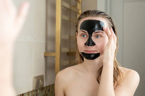 Жінка з очищаючою чорною маскою на обличчі у ванній — стокове фото