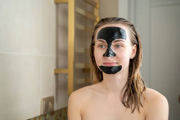Жінка з очищаючою чорною маскою на обличчі у ванній — стокове фото