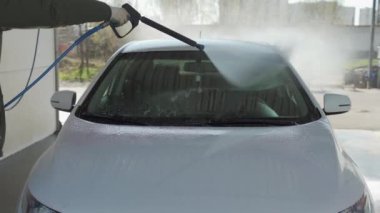 Bir adam oto yıkamada araba yıkıyor yüksek basınçlı araç yıkama makinesi suyla temizleniyor. Araba yıkama ekipmanı