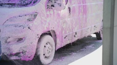 Araba yıkamada köpükle kaplanmış bir otomobil. Araba yıkama işçisi arabaya köpük sürüyor.