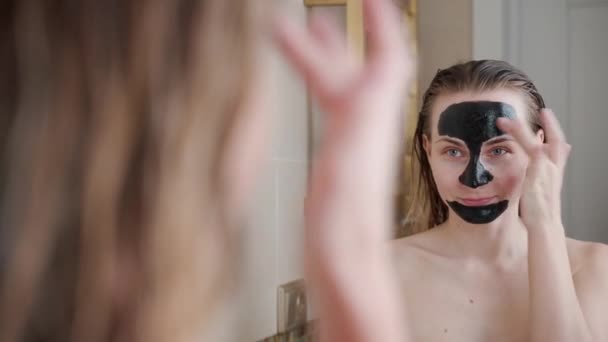 Young woman puts a black beauty mask on her face — 비디오