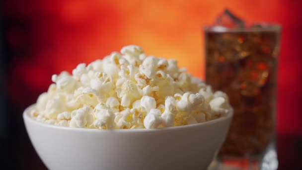 Mano prende popcorn da una ciotola bianca sullo sfondo di un bicchiere di cola . — Video Stock