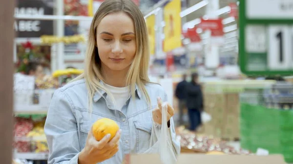 Młoda kobieta wybiera świeżą pomarańczę w sklepie spożywczym. — Zdjęcie stockowe