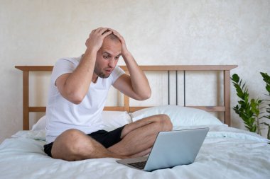 Yatak odasındaki bir yatakta dizüstü bilgisayarla çalışan bir adam için maddi kayıplar.