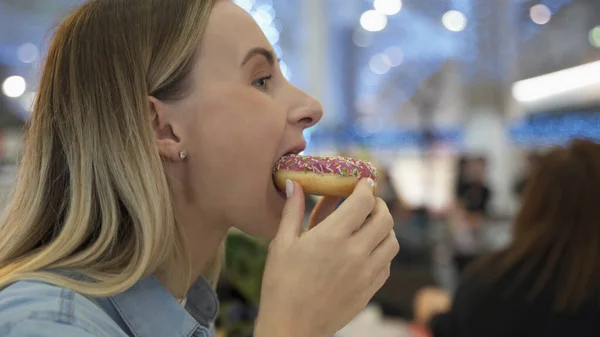 Mujer joven comiendo donut en el centro comercial — Foto de Stock